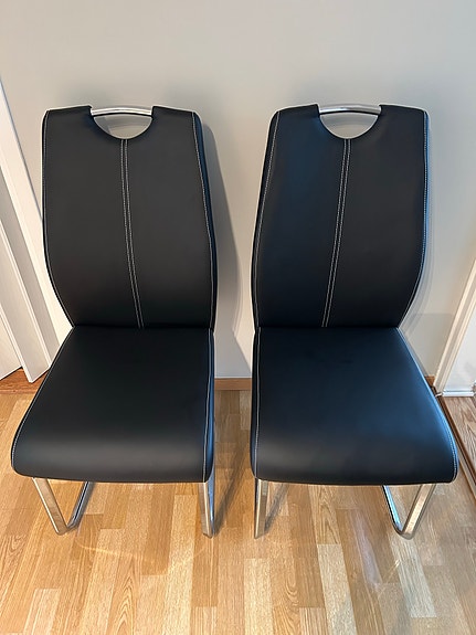 2 svarta stolar i läderlook och stålben